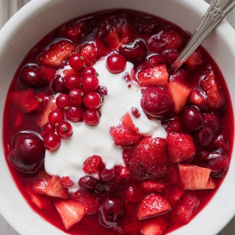 Vibrante rote Beerensüßspeise, serviert in Gläsern mit Sahne.  